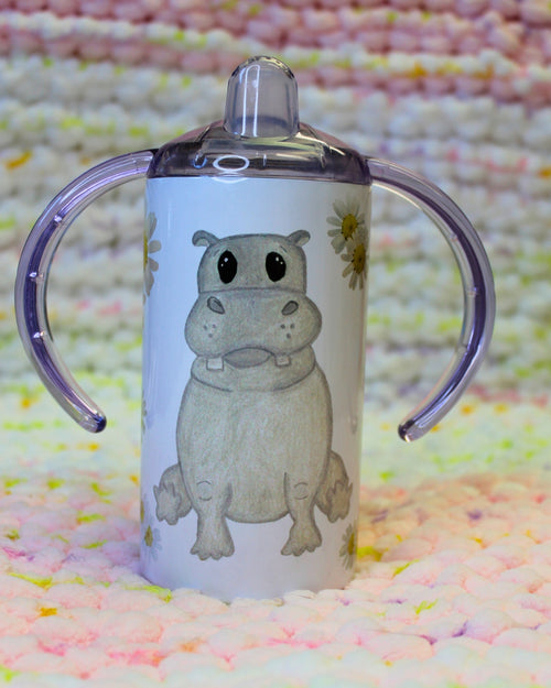 Hand-drawn cartoon gray hippo sitting, surrounded by daisy flowers on a white sippy cup.