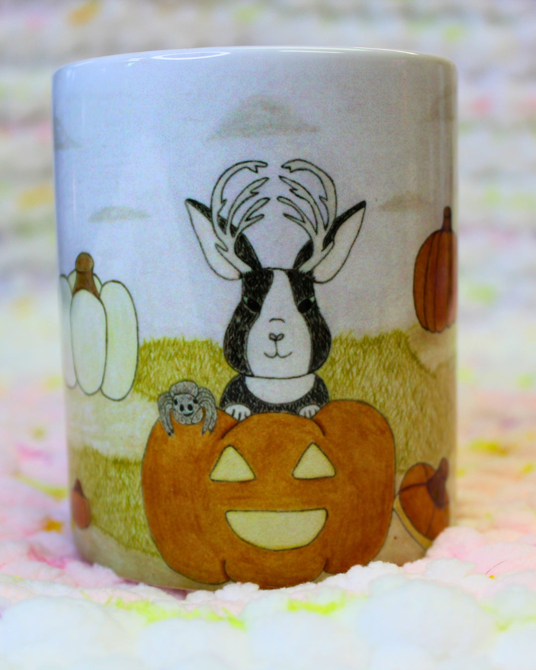 Hand-drawn cartoon Jackalope in a jack-o’-lantern, with a jumping spider friend in a pumpkin patch, on a ceramic mug.