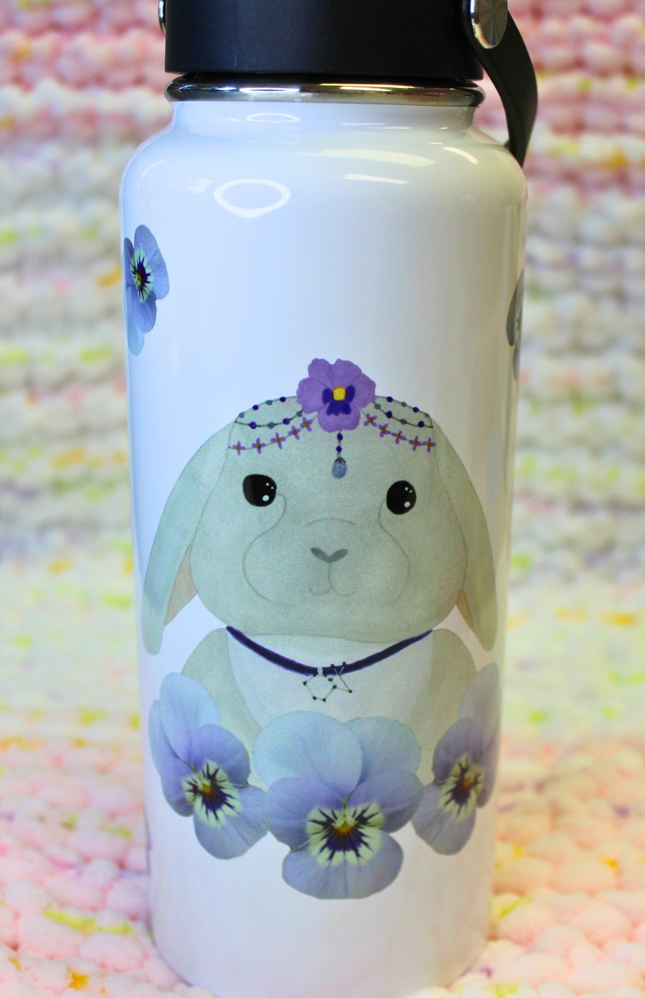 Cartoon gray lop-eared bunny, wearing fancy head jewelry and a rabbit constellation necklace, and surrounded by pansies, on a hydro-style tumbler.
