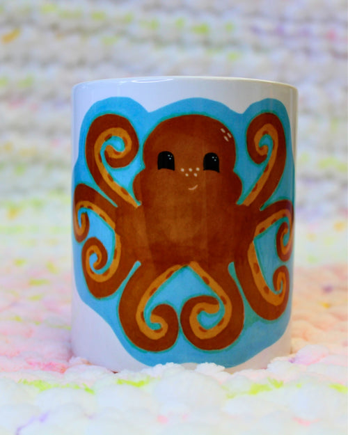 Hand-drawn happy orange cartoon octopus with heart-shaped tentacles, surrounded by blue water, on a ceramic mug.